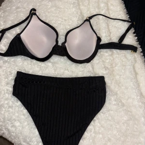 Svart ribbad bikini set - Snygg svart bikini med ribbad struktur. Överdelen har justerbara axelband och bygel för extra stöd. Underdelen är klassisk i snittet och matchar perfekt med överdelen. Perfekt för en dag på stranden eller vid poolen.