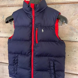 RALPH LAUREN VÄST - Säljer nu min Ralph lauren väst, västen är använd men i mycket fint skick, västen är ”reverisble” vilket gör att du kan använda både röd och blå. Nypris på västen är ca  2500kr. Västens storlek är barn 10-12 år skulle säga att den passar bra till XS