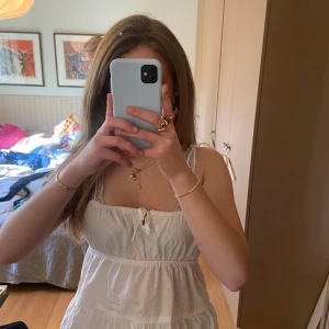 Vit ärmlös linnetopp - Säljer en söt vit ärmlös linnetopp med smala axelband och knytning framtill. Toppen har en luftig och lätt design, perfekt för varma dagar.