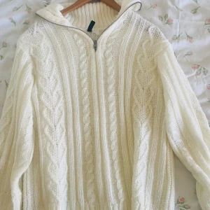 Vit stickad tröja med dragkedja från H&M Divided - Säljer en vit stickad tröja från H&M Divided med dragkedja och kabelstickat mönster. Tröjan har en hög krage och långa ärmar, perfekt för kyliga dagar. Mysig och stilren design som passar till mycket. 🧶✨