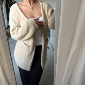 Beige stickad kofta - Mysig beige stickad kofta med långa ärmar och två fickor framtill. Perfekt för kyliga dagar och ger en avslappnad look. Passar bra över en enkel topp eller t-shirt.