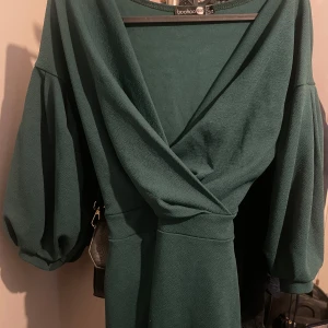 Grön omlottklänning från Boohoo - Snygg grön omlottklänning från Boohoo med v-ringning och trekvartsärmar. Perfekt för en stilren look. Klänningen har en elegant passform och är tillverkad i ett mjukt material.