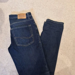Mörkblå jeans från Jack & Jones - Snygga mörkblå jeans från Jack & Jones med klassisk femficksdesign. De har en slim passform och är perfekta för en stilren look. Märkeslappen i läder sitter baktill vid midjan.
