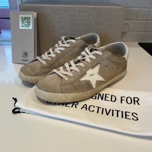 Beige sneakers från Golden Goose - Sperfräsha Golden goose superstar i beige med klassiska golden goose slitningar. Skorna är i storlek 41 men passar som 42. Skorna är i mocka och blir perfekt till sommaren! Allt og medföljer, Hör av dig vid minsta fundering ⭐️