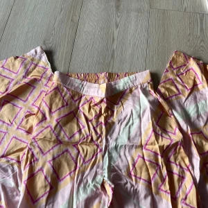 Mönstrade byxor från Öster Enhagen - Säljer ett par färgglada byxor från Öster Enhagen med ett unikt mönster i rosa och gult. Byxorna har en elastisk midja för extra komfort och är perfekta för en avslappnad stil. Passar bra till både vardag och speciella tillfällen.🩷