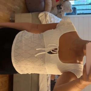 Vit spetsblus med knyt från Nelly - Supersöt vit blus från Nelly med broderade detaljer och lätt spetskänsla. Toppen har korta, lite fladdriga ärmar och en snygg knytning framtill vid den djupa, rundade urringningen. Perfekt för en fräsch och somrig look! Storlek M men skulle säga att den är väldigt liten i storlek, så passar även S💞