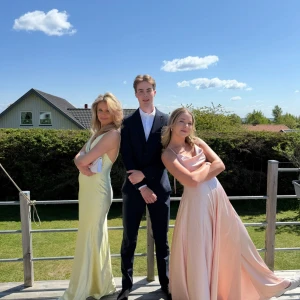 Ljusrosa långklänning med smala axelband - Superfin ljusrosa långklänning i satin med smala axelband och draperad urringning. Klänningen har en flowy kjol och sitter snyggt i midjan. Perfekt för bal eller student! Säljer då jag inte längre behöver den.