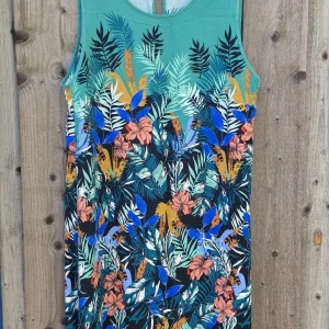 Blommig ärmlös klänning från Indiska - Färgstark ärmlös klänning från Indiska med tropiskt blommönster i grönt, blått, orange och svart. Mjuk bomullskänsla, rund hals och knäppning bak i nacken. Perfekt för dig som gillar statement-plagg och vill sticka ut i sommar. Materialet 100 % Viskos