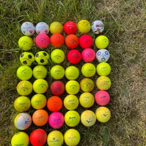 Pro v1, tp5, chrome soft - Bilden visar en samling färgglada golfbollar av olika märken och färger, upplagda på gräs. Det finns ingen bok på bilden.