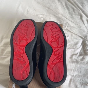Christian Louboutin svarta sneakers mocka - Exklusiva svarta sneakers från Christian Louboutin i mjuk mocka med klassisk röd sula och snörning. Snygg och stilren design med rund tå och diskreta detaljer. Kommer med originalkartong och dustbag.