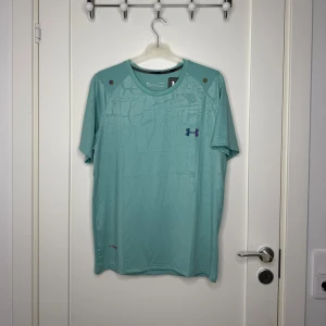 Under Armour träningströja herr i turkos – stl M - Superskön träningströja från Under Armour i fräsch turkos färg med diskret mönster. Storlek M. Perfekt för löpning, gym eller annan träning tack vare det snabbtorkande materialet. I mycket fint skick utan fläckar eller hål. 🧼 Oanvänd 📦 Skickas snabbt 👕 Passar dig som gillar sportiga och funktionella plagg