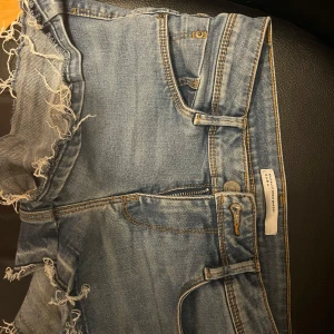 Lågmidjade jeansshorts från Zara Trafaluc - Snygga blå jeansshorts från Zara Trafaluc i storlek 34. Klassisk femficksmodell med fransiga kanter och slitna detaljer för en cool vibe. Shortsen har en låg midja och är perfekta för varma dagar. Dragkedja och knapp framtill.