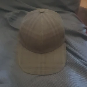 Äkta burberry keps - Snygg rutig keps från Burberry i dova grå och beige toner. Klassisk böjd skärm, justerbart spänne bak med metallspänne och broderad Burberry-logga. Tillverkad i 100% bomull för en skön och stilren look.