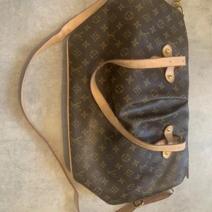 monogram axelväska - Säljer en klassisk axelväska i brunt med ikoniskt monogrammönster och ljusa skinnhandtag. Väskan har guldfärgade metalldetaljer, dragkedja och rymligt innerfack med logotypmönster. Perfekt för dig som vill ha en statementväska med lyxig känsla. Det är bara en sak och det är att en av dragkedjorna är trasig 