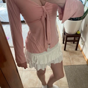 Rosa omlottopp med knyt och trumpetärm - Supersöt rosa omlottopp med knyt framtill och v-ringning. Toppen har långa trumpetärmar och är figurnära i modellen. Perfekt för dig som gillar en feminin och trendig stil. Mjuk och skön i materialet.