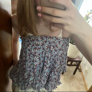 Blommig blå bandeau tubtopp - Du kan också att bära som kjol. Supersöt bandeau tubtopp i ljusblått med blommigt mönster i lila och vitt. Toppen är luftig och har volangkant nertill, perfekt för varma dagar. Sitter offshoulder och är ärmlös, med en flowy och avslappnad passform.