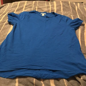 Blå t-shirt från Amisu - Enkel blå t-shirt från Amisu i mjuk bomull. Klassisk rund halsringning och korta ärmar. Perfekt basic-plagg att ha i garderoben, lätt att matcha med jeans eller shorts. Snygg och stilren utan tryck eller mönster.