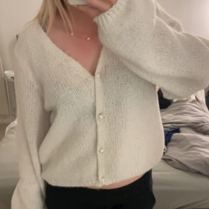 Vit stickad kofta med pärlknappar - Superfin vit stickad kofta med v-ringning och pärlknappar framtill. Koftan har en lite loose passform och långa ärmar, perfekt att slänga på sig över ett linne eller t-shirt. Enkel och stilren, passar till allt.