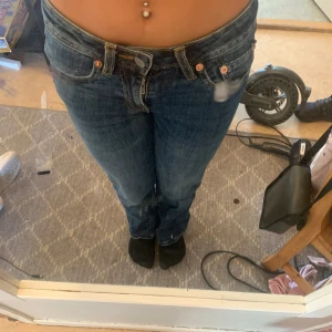 Blåa jeans med fickor  - Säljer ett par klassiska blå jeans från 7 For All Mankind med raka ben och låg midja. Jeansen har snygga detaljer på bakfickorna och en mörk tvätt. Perfekta för dig som gillar en tidlös och avslappnad look.