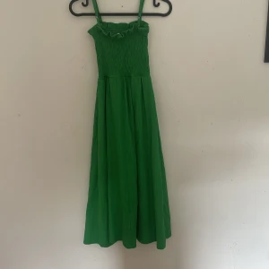 Grön långklänning från H&M XS - Snygg grön långklänning från H&M i storlek XS. Klänningen har smockad överdel, smala axelband och en flowy kjol. Perfekt för varma dagar och somriga vibes. Materialet känns lätt och luftigt.