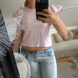 Ljuslila croppad blus med volangärm - Supersöt ljuslila blus med croppad passform och volangiga korta ärmar. Perfekt för dig som gillar en feminin och trendig stil. Tunn och skön bomull som passar till både jeans och kjol.