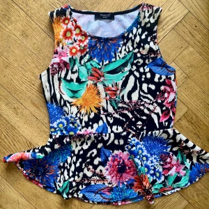 Blommig peplumtop från Sisters Point - Färgstark peplumtop från Sisters Point med blommigt och zebramönster i blått, orange, rosa, grönt och svart. Toppen är ärmlös och har rund halsringning. Materialet är stretchigt och bekvämt, perfekt för dig som vill sticka ut.