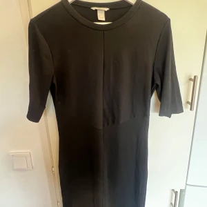 Svart enkel kortklänning H&M - Svart, stilren kortklänning från H&M med rund halsringning och halvlånga ärmar. Klänningen har en rak passform och är tillverkad i ett mjukt, stretchigt material som känns bekvämt mot huden. Perfekt för dig som gillar minimalistisk stil✨