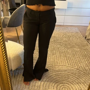 Svarta lågmidjade bootcut kostymbyxor - Säljer ett par svarta kostymbyxor med bootcut passform och låga i midjan. Byxorna har slits. Säljs då jag har rensar garderoben 
