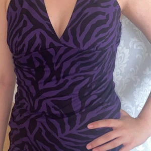Lila zebramönstrad topp  - Säljer en snygg topp med lila och svart zebramönster. Plaggen har en djup v-ringning och figurnära passform, perfekt för dig som vill sticka ut. Materialet känns mjukt och stretchigt, vilket gör den bekväm att bära hela kvällen.