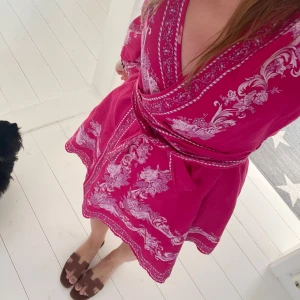 Sommarklänning - Superfin rosa kortklänning i omlottmodell med vita blommiga detaljer. Klänningen köptes på jackie från märket Love lolina.