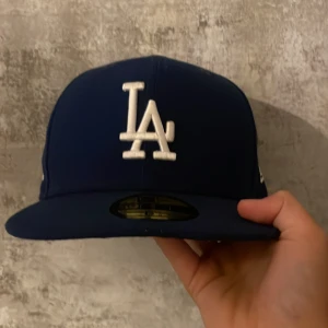 Blå LA Dodgers keps från New Era - Snygg mörkblå LA Dodgers keps från New Era med broderad vit LA-logga framtill, köpte för 700kr, MLB-logga bak och New Era-logga på sidan. Kepsen är design av Milton keynes kan skicka bild ifall ni vill ha på det. Väldigt bra kvalité😊