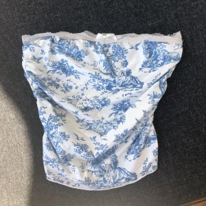 Vit blå topp med spets - Supersöt  topp i vitt med blått mönster och spetskant upptill. Toppen har rynkade sidor som ni ser på sista bilden, så den är stretchig. Den är S men passar XS M S. 