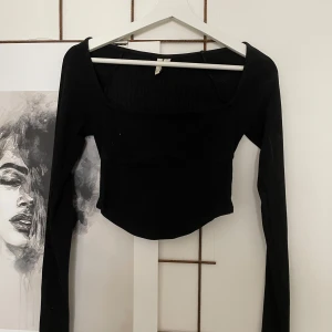 Svart ribbad croppad topp NLY Trend - Svart långärmad croppad topp från NLY Trend med fyrkantig urringning och ribbad struktur. Sitter tight och har en markerad söm under bysten för extra detalj. 