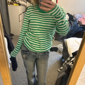 Grönvit randig stickad tröja - Säljer en grön och vit randig stickad tröja med lång ärm och rund hals. Tröjan har en slim passform och är perfekt för dig som gillar färg och mönster. Superenkel att styla med jeans eller kjol för en cool vardagslook.