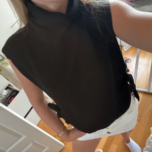 Svart stickad väst med knytning vid höfterna från Visual Clothing Project - Svart stickad väst med knytning vid höfterna. Perfekt till en fin och lite kall höstdag. Väldigt mysig! Polo krage. 