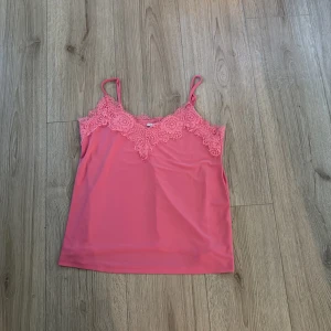 Rosa linnetopp med spets från Amisu - Supersöt rosa linnetopp från Amisu med tunna axelband och v-ringning dekorerad med blommig spets. 