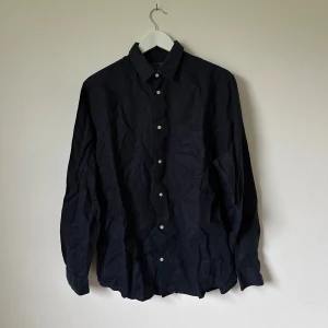 Mörkblå linneskjorta från H&M, M - Svart mörkblå från H&M i 100% linne. Klassisk modell med krage, bröstficka och vita knappar framtill. Långärmad och perfekt för en stilren look. Skjortan har en avslappnad passform och är riktigt skön under varmare dagar. Artnr: B350