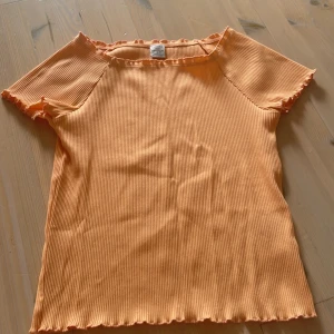 Ribbad orange topp från Lindex - Superfin ribbad topp i ljus orange från Lindex med korta ärmar och volangkant vid hals, ärmslut och nederkant. Från Lindex,  och säljs inte längre💗