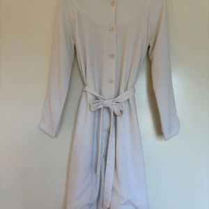 Vit Rodebjer kappa med bälte och sidofickor, XS - Superfin vit kappa från Rodebjer i storlek XS. Kappan har långa ärmar, knappar fram och ett bälte i midjan. Tillverkad i en mjuk mix av återvunnen polyester, viskos och elastan. Jättefint skick men har dragit sig lite i tvätten nedtill - därav lågt pris!