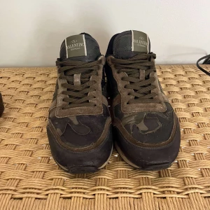 Valentino Garavani Rockrunner sneakers - Snygga Valentino Garavani Rockrunner sneakers i mörkgrönt och brunt med camouflage-mönster. Skorna har detaljer i mocka, skinn och textil, samt coola nitar på sulan. Klassisk snörning och unik design som sticker ut.