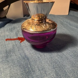 Lila parfymflaska med silverdetaljer - Unik parfymflaska i lila glas med rund form och lyxigt silverfärgat lock. Locket har detaljer i relief och en konformad topp som ger en cool och exklusiv känsla. Perfekt som statement på sminkbordet eller i samlingen.