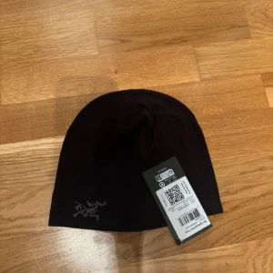 Svart mössa från Arc'teryx - Svart mössa från Arc'teryx med stilren broderad logga i vitt framtill. Tillverkad i mjukt och stretchigt material som sitter skönt på huvudet. Perfekt för kyliga dagar och outdoor-aktiviteter.