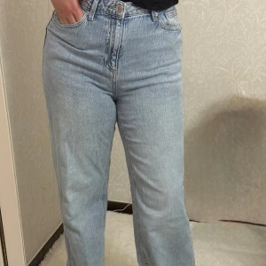 Ljusblå baggy  jeans med hög midja - Säljer ett par ljusblå jeans med hög midja och raka ben. Jeansen har klassisk femficksdesign, gylf med dragkedja och knapp samt en avslappnad passform. Perfekta för en chill och trendig look. 