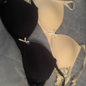 2-pack bh toppar Laura Ashley 30A - Säljer två bh toppar från Laura Ashley i storlek 30A. En är svart och en är beige, båda med spetsdetaljer på sidorna och små rosetter framtill. Tillverkade i mjuk bomullsmix med 95% bomull och 5% spandex för extra stretch och komfort. 