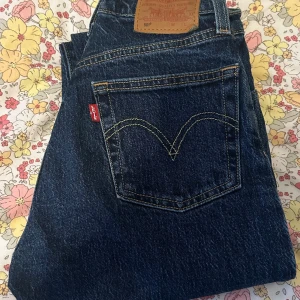 Levi's 501 mörkblå jeans straight fit - Klassiska Levi's 501 jeans i mörkblå denim med raka ben och hög midja. Snygga kontrastsömmar, femficksmodell och ikonisk röd Levi's-tag på bakfickan. Tillverkade i slitstarkt bomullstyg, perfekt för en tidlös look.