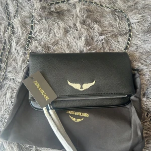 Svart axelväska från Zadig & Voltaire - Snygg svart axelväska från Zadig & Voltaire med guldfärgade detaljer och kedjerem. Har inget bevis att väskan är äkta. Köpte den på plick hon sa den var äkta. Men jag säljer då den it var min stil. 