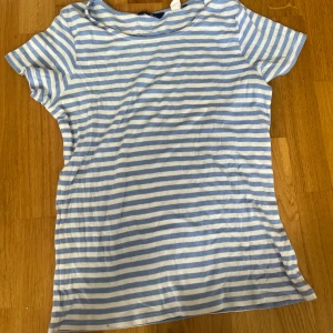 Blåvit randig t-shirt från GANT - Snygg blåvit randig t-shirt från GANT med broderad logga på bröstet. Klassisk passform och korta ärmar, perfekt för en chill och stilren look. Tillverkad i mjuk bomull som känns skön mot huden.