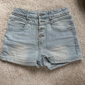 Högmidjade ljusa jeansshorts - Säljer dessa snygga shorts med fina knappar. Ostrechat är midjemåttet 30 rakt över. Uppskattat xxs-xs. Annars barnstorlek.