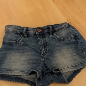 Blå jeansshorts  - Snygga blå jeansshorts med klassisk femficksdesign och knappgylf. Perfekta för sommardagar och avslappnade stunder. De har en lätt tvättad look som ger en cool och avslappnad stil.