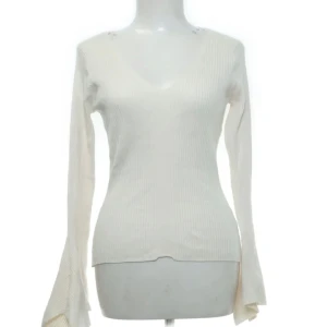 Vit ribbad tröja med v-ringning - Säljer en stilren vit ribbad tröja med v-ringning och långa ärmar ifrån River Island. Tröjan har en figurnära passform och är perfekt för en elegant look då den har vida armar. Den är tillverkad i ett mjukt material som ger en bekväm känsla.